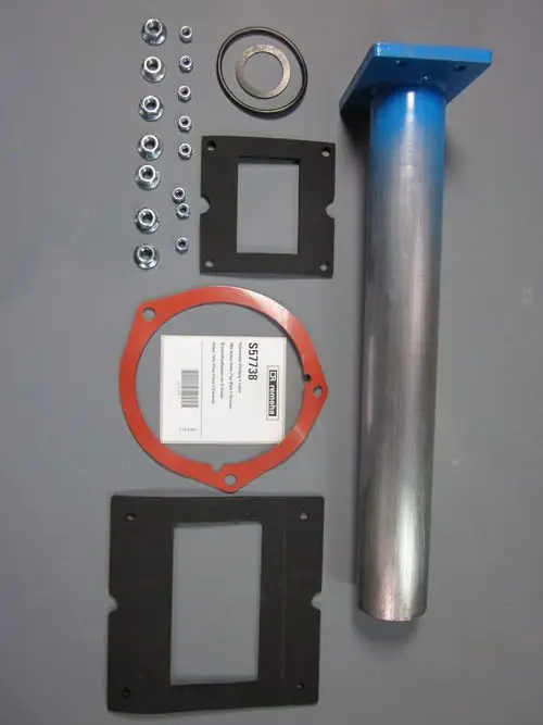 Remeha Zubehörset mit einem Metallrohr, Dichtungen, Unterlegscheiben und Schrauben, angeordnet auf grauer Unterlage.